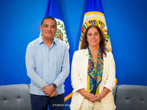 Francis Fonseca standing beside a visiting representative in front of the flags of Belize and the Organization of American States.