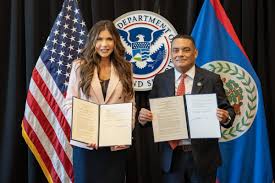 Francis Fonseca and a United States official each holding an open signed folder before the flags of the United States, the Department of Homeland Security and Belize.
