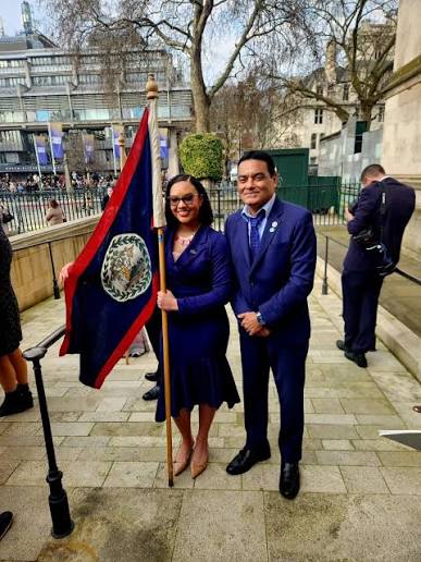 Francis Fonseca standing outdoors in London beside a colleague carrying the national flag of Belize on a staff, ahead of a ceremonial occasion.
