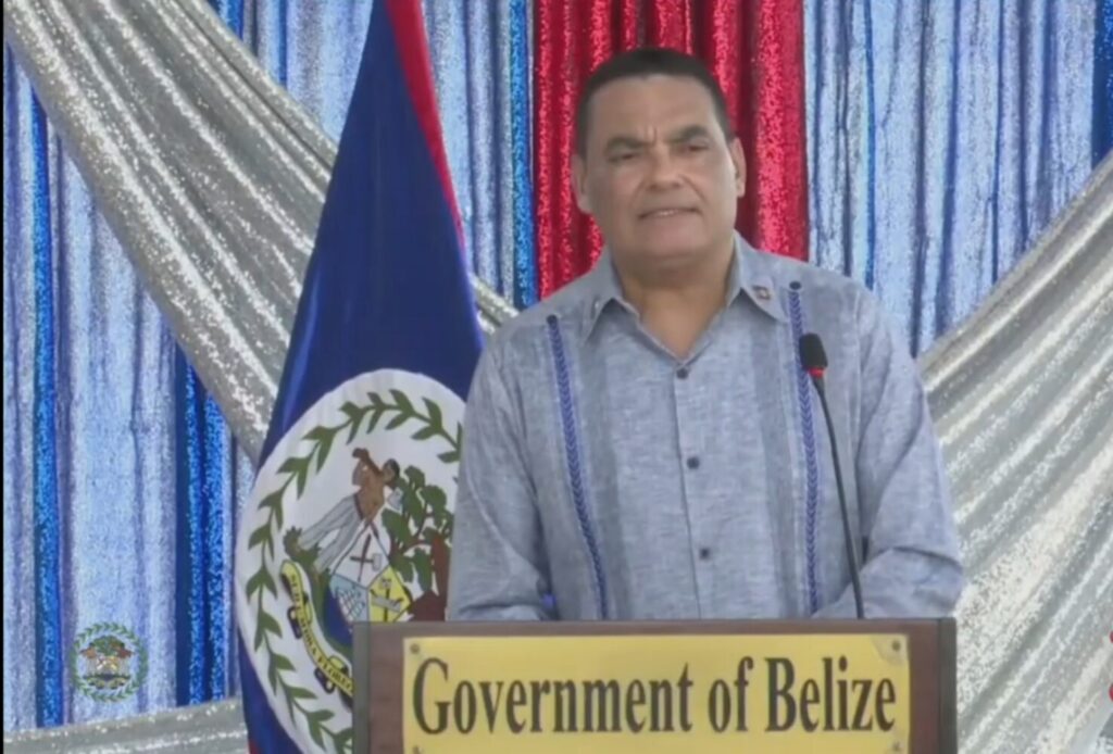Francis Fonseca speaking from a lectern marked Government of Belize, with the national flag beside him.