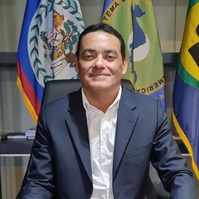 Francis Fonseca seated at his office desk in front of the flags of Belize, the Central American Integration System and the Caribbean Community.