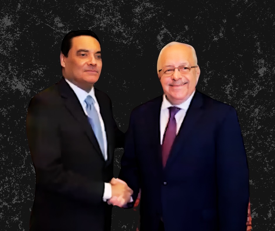 Francis Fonseca in a dark suit shaking hands with another official, both facing the camera against a dark background.