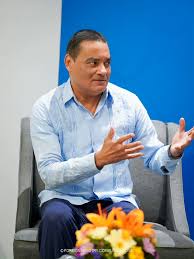Francis Fonseca seated in an armchair, both hands raised mid-sentence during a conversation.